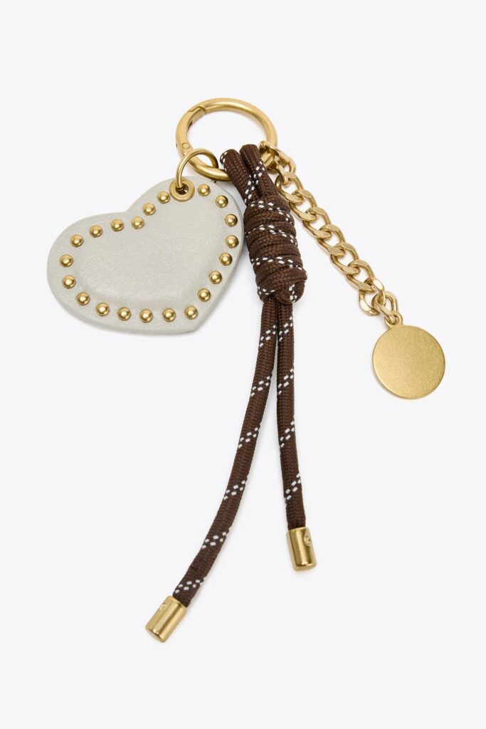 Heart-shaped charm with gold studs, chain, and brown cord with white details.