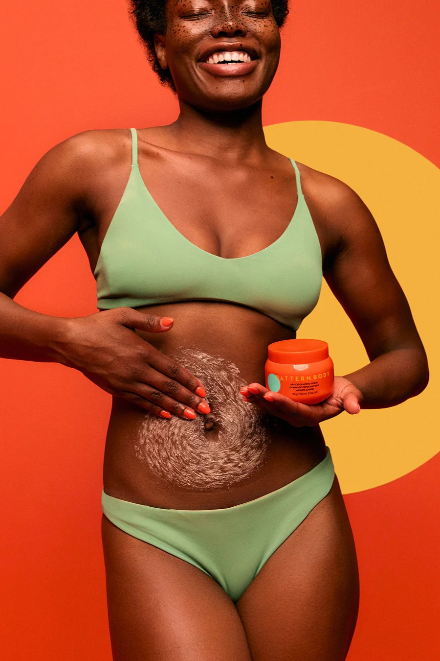 Model Holding Dry Exfoliating Body Scrub and using it on her belly