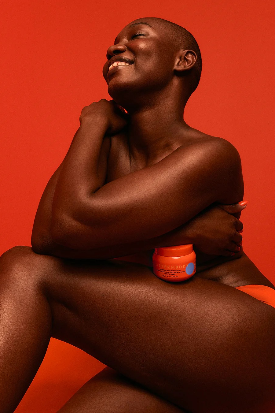 Model Holding Pattern Moisture Rich Body Cream with Orange Background